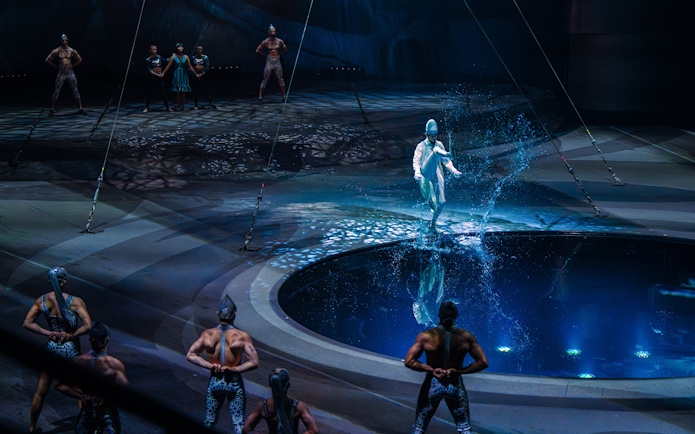 Performer at La Perle show in Dubai walking on water with acrobats in the background.