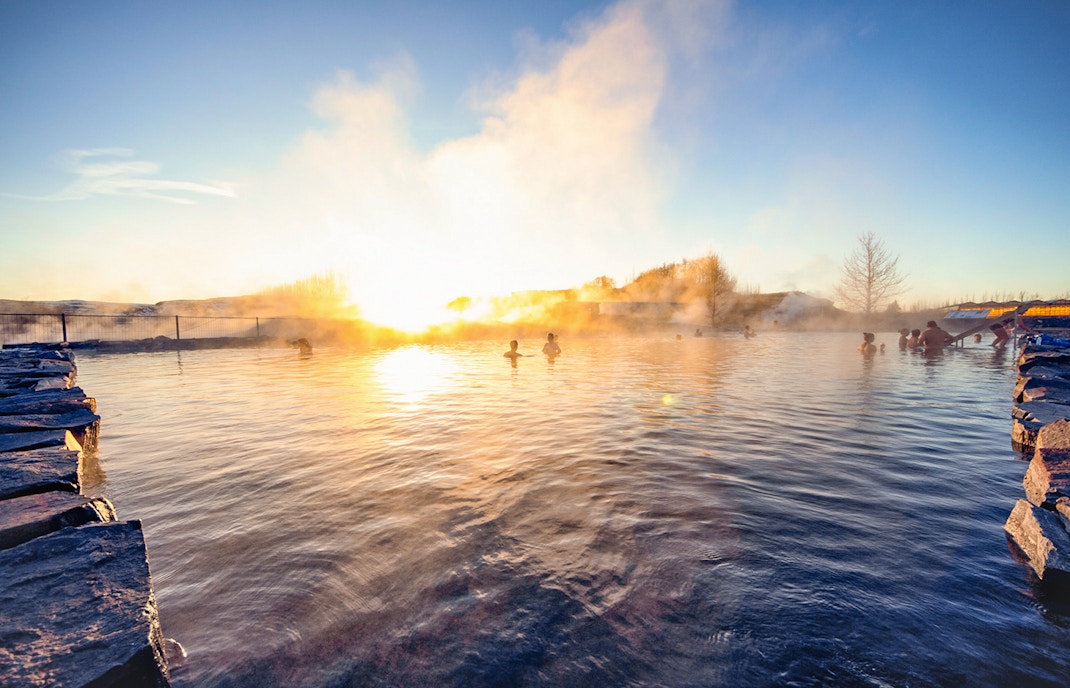 Reykjavik Secret Lagoon geothermal pool with steam rising, surrounded by natural landscape.