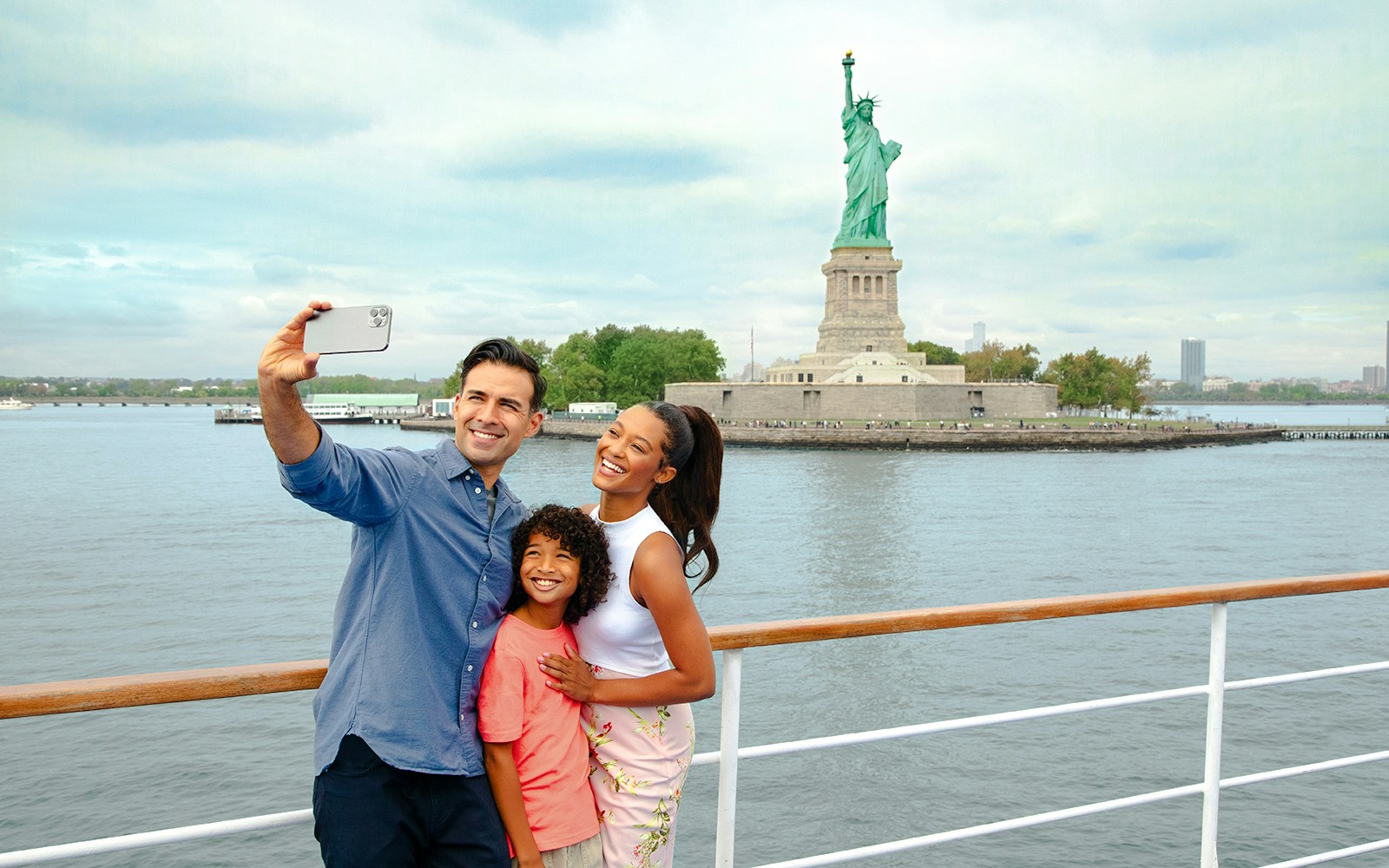 Family taking a selfie on a luxury glass boat with the Statue of Liberty in the background.