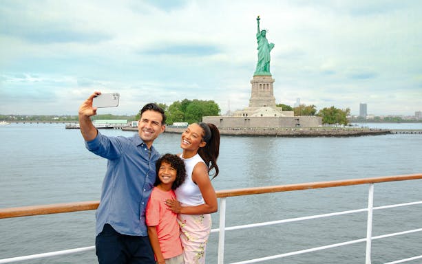 Family taking a selfie on a luxury glass boat with the Statue of Liberty in the background.