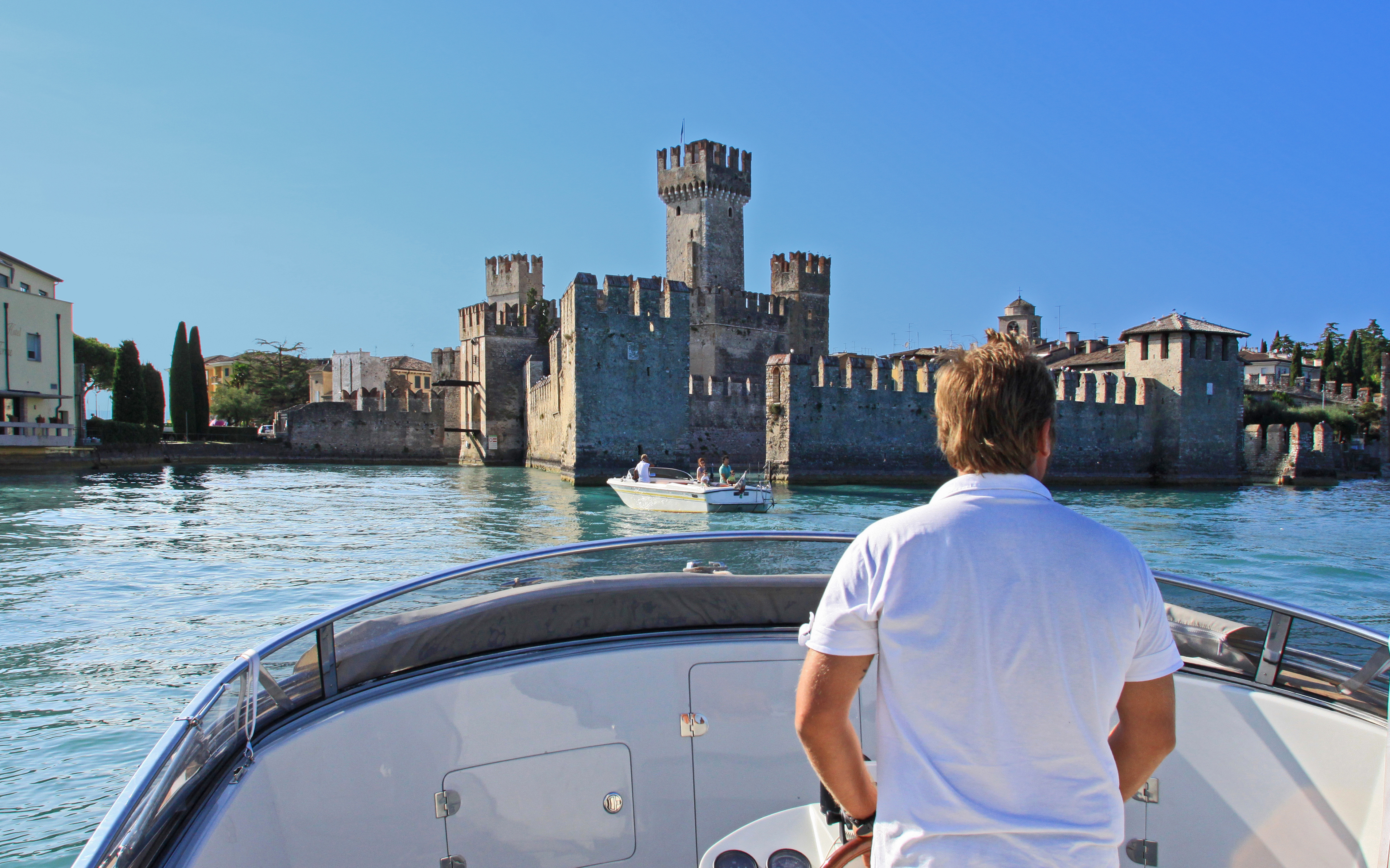 Boat approaching Scaliger Castle in Sirmione, Italy, with a view of the castle's towers and walls.