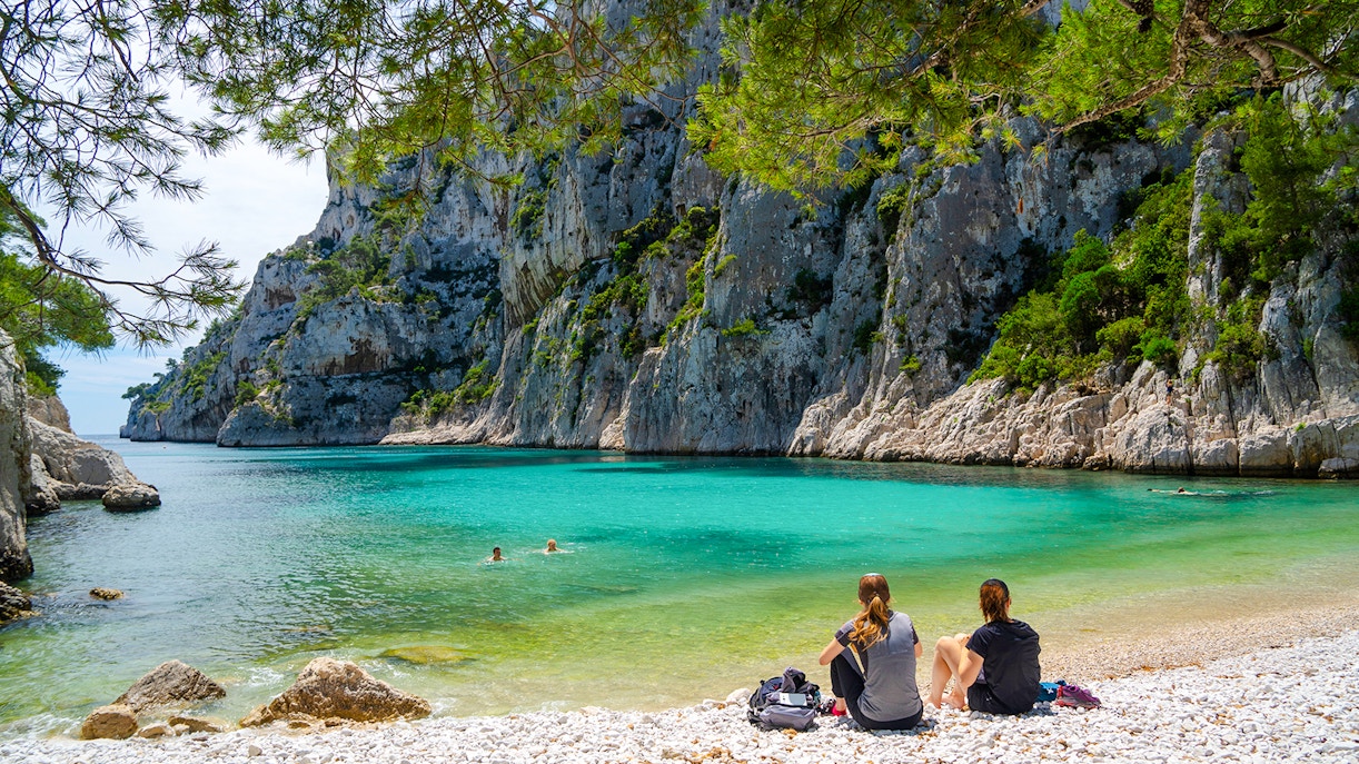 Visitors relaxing by turquoise waters and cliffs at Calanques National Park, France.