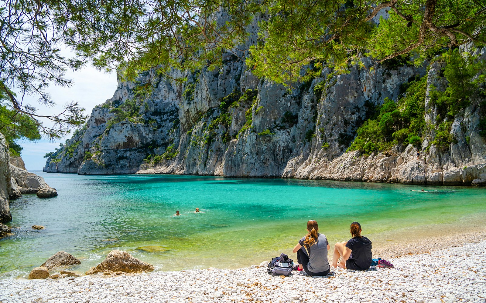 Visitors relaxing by turquoise waters and cliffs at Calanques National Park, France.