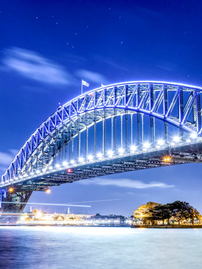 Sydney Harbour Bridge illuminated at night over the water.