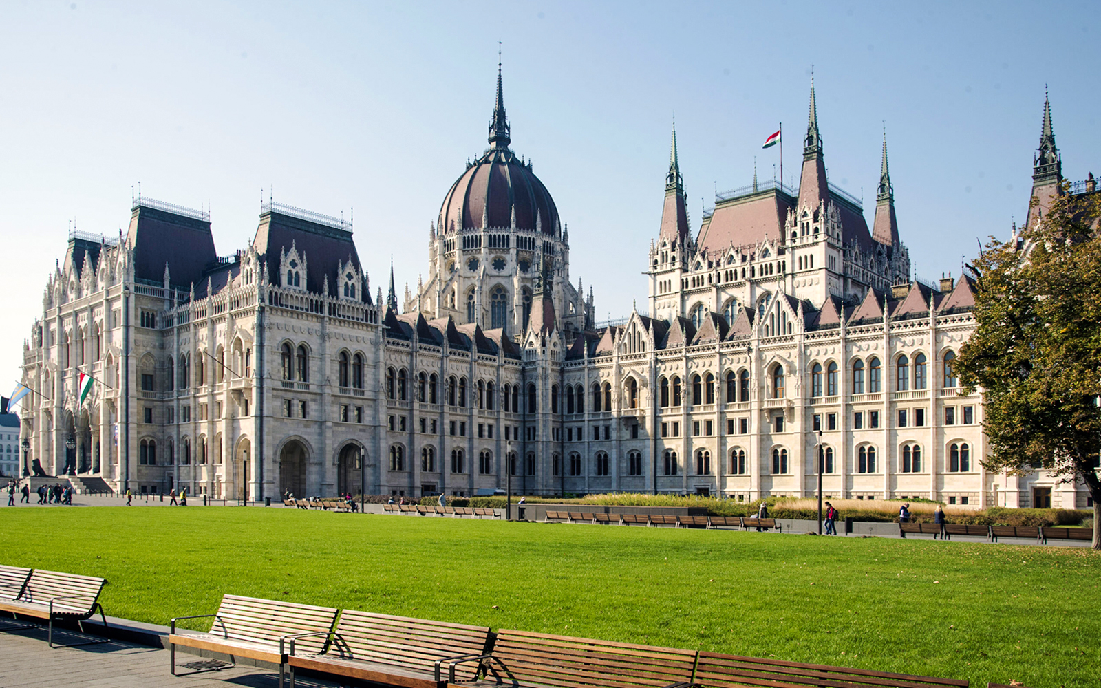 Hungarian Parliament Building in Budapest with green lawn and benches in foreground.