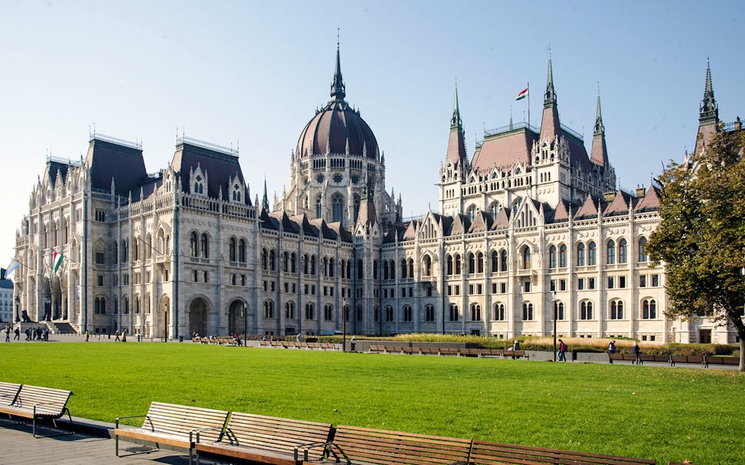 Hungarian Parliament Building in Budapest with green lawn and benches in foreground.