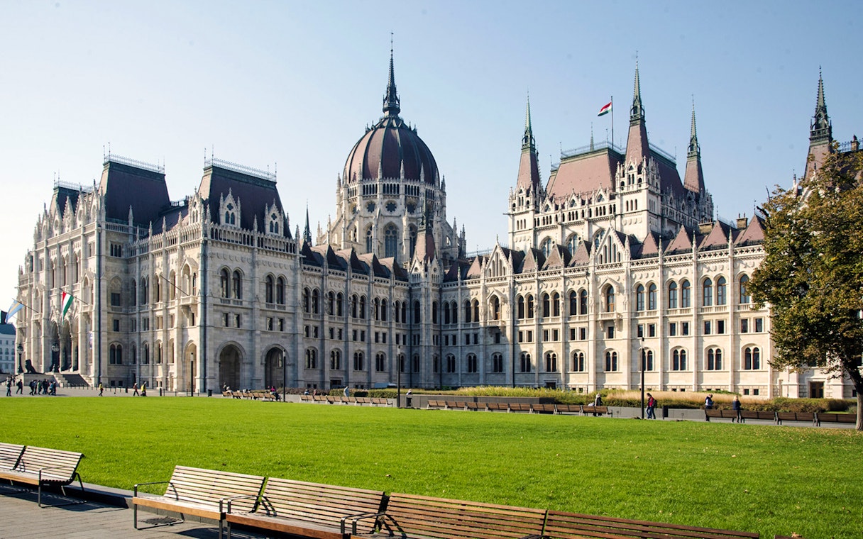 Hungarian Parliament Building in Budapest with green lawn and benches in foreground.