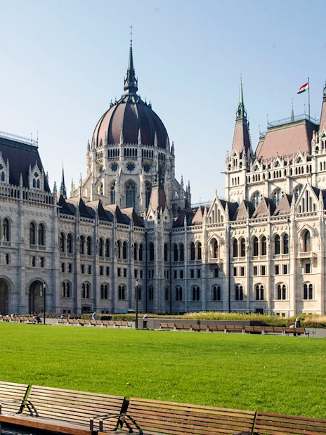 Hungarian Parliament Building in Budapest with green lawn and benches in foreground.