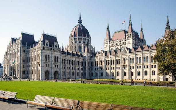 Hungarian Parliament Building in Budapest with green lawn and benches in foreground.