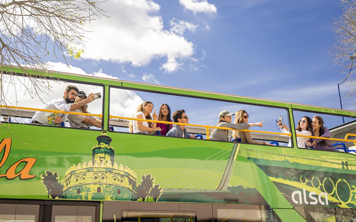 Tourists on Seville hop-on hop-off bus taking photos and enjoying city views.
