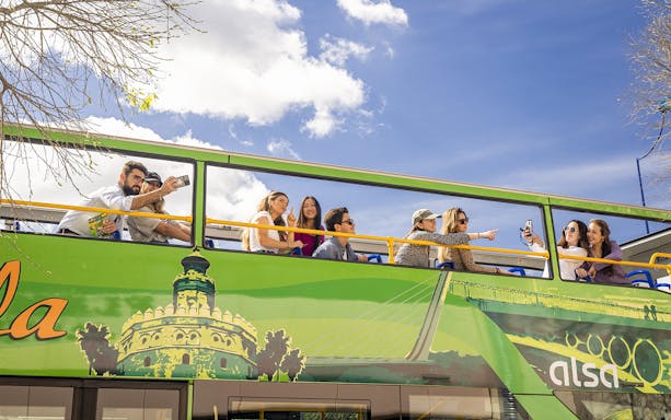 Tourists on Seville hop-on hop-off bus taking photos and enjoying city views.