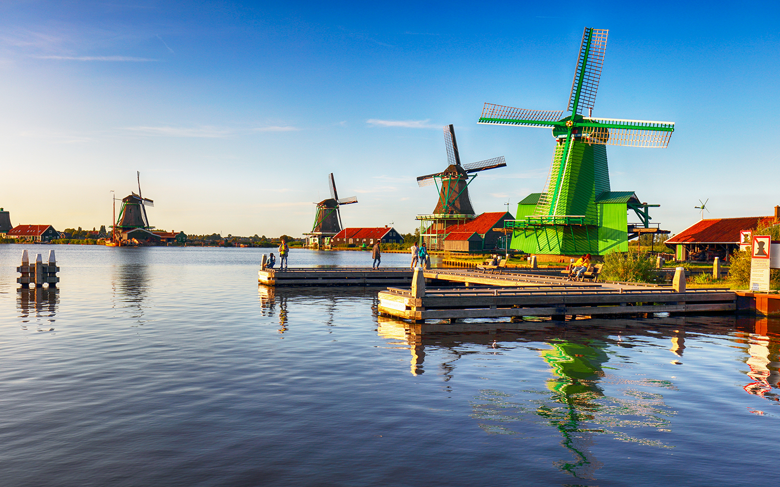 Windmills at Zaanse Schans near Amsterdam with people on a dock.