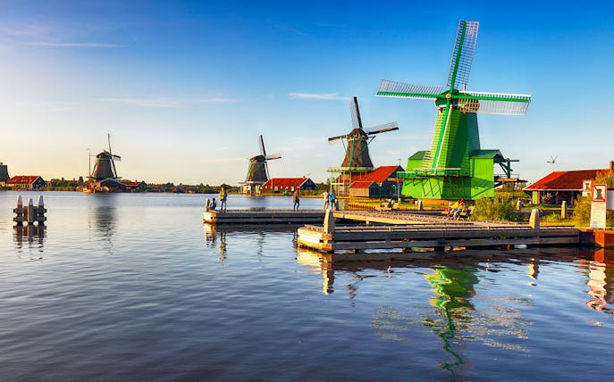 Windmills at Zaanse Schans near Amsterdam with people on a dock.