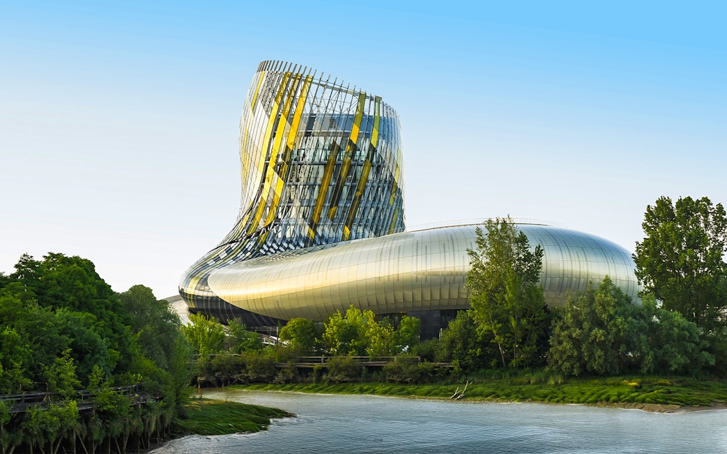 Cite du Vin viewed from Bordeaux river cruise, modern architecture surrounded by trees.