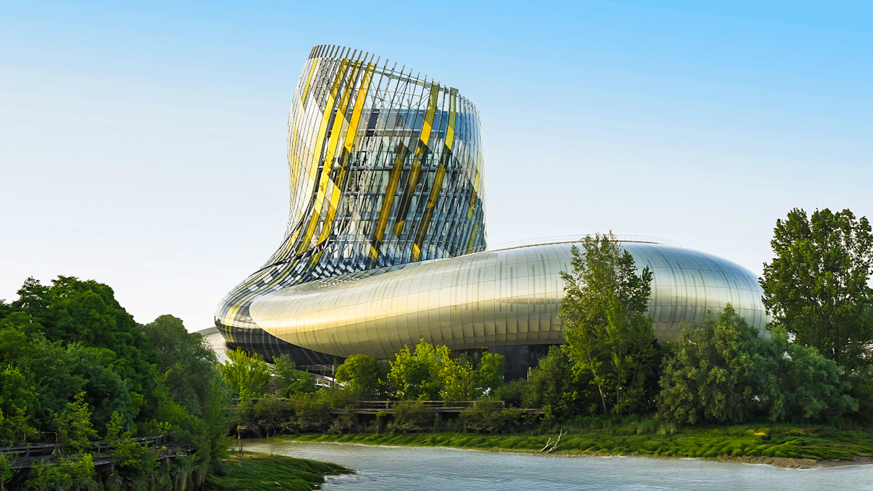 Cite du Vin viewed from Bordeaux river cruise, modern architecture surrounded by trees.