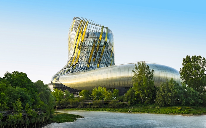 Cite du Vin viewed from Bordeaux river cruise, modern architecture surrounded by trees.