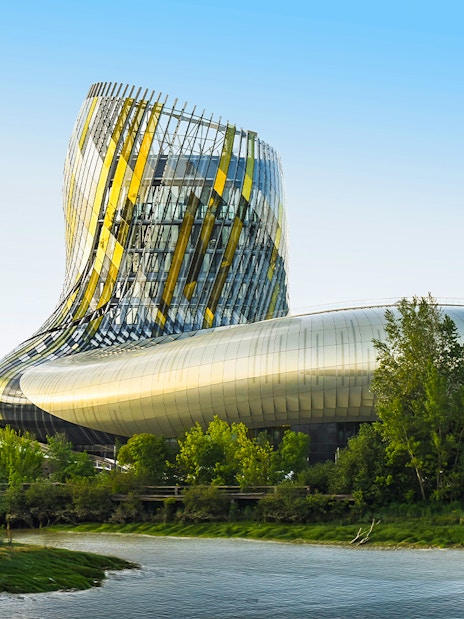 Cite du Vin viewed from Bordeaux river cruise, modern architecture surrounded by trees.