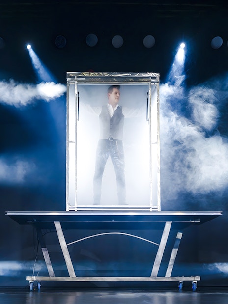 Illusionist performing in a glass box with stage lights at the Evolution Magic Show.