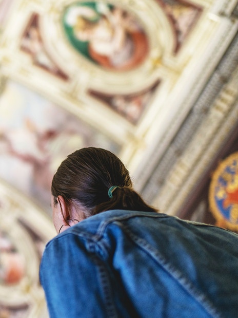 Visitor admiring ceiling artwork in the Vatican Museums.