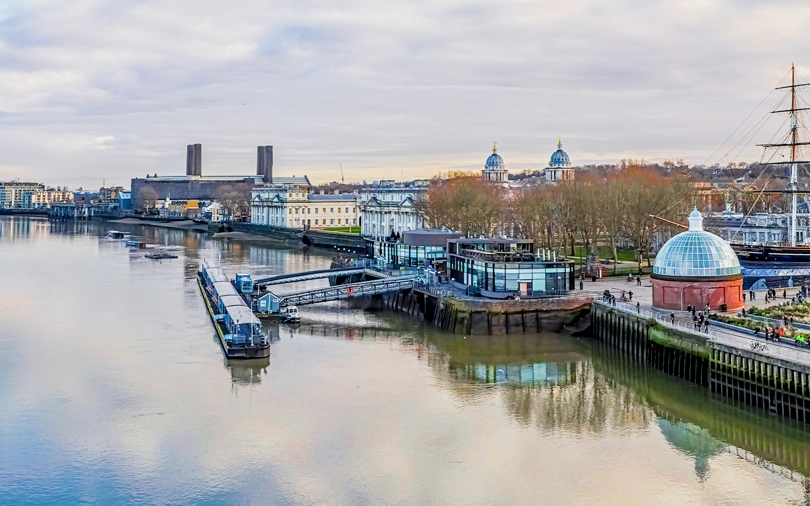 Greenwich Pier on the Thames River with historic buildings and Cutty Sark ship.