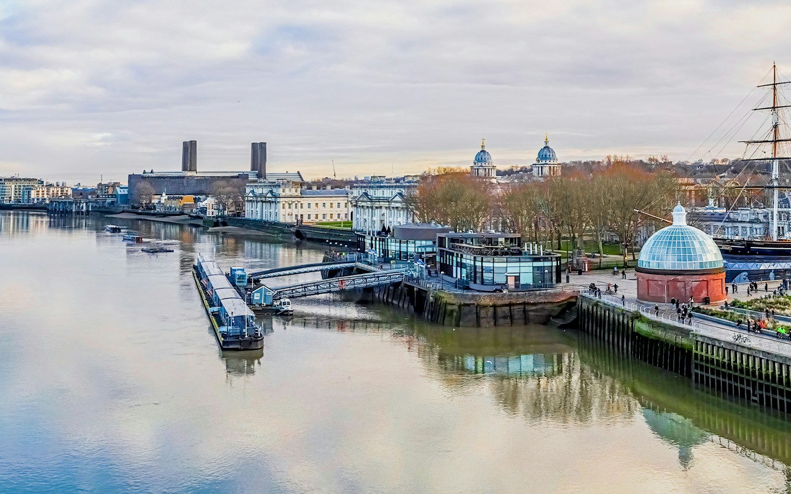 Greenwich Pier on the Thames River with historic buildings and Cutty Sark ship.
