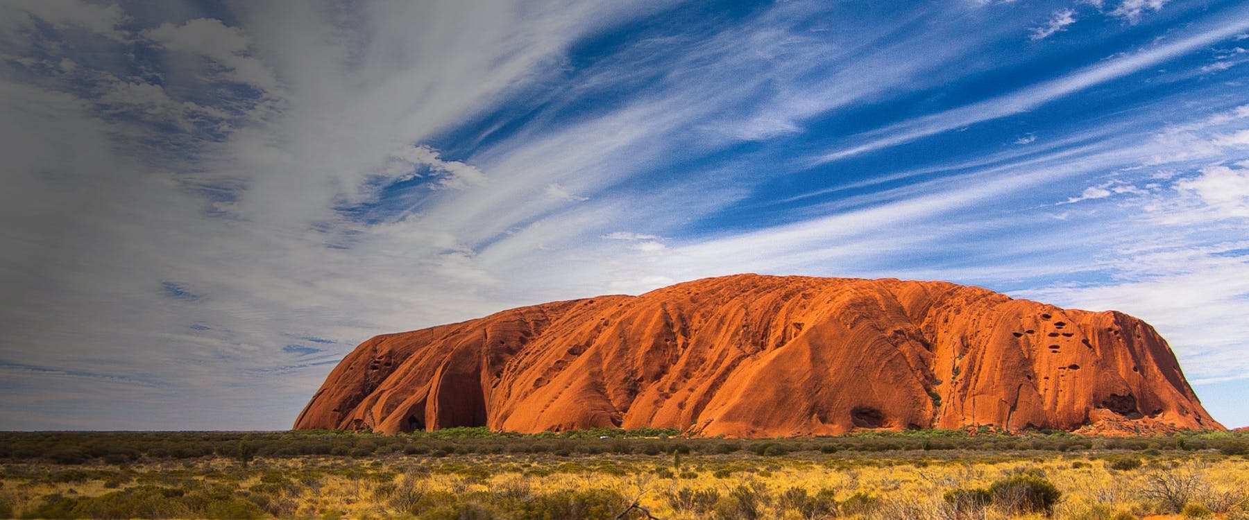 Uluru rock formation under a blue sky in Yulara, Australia.