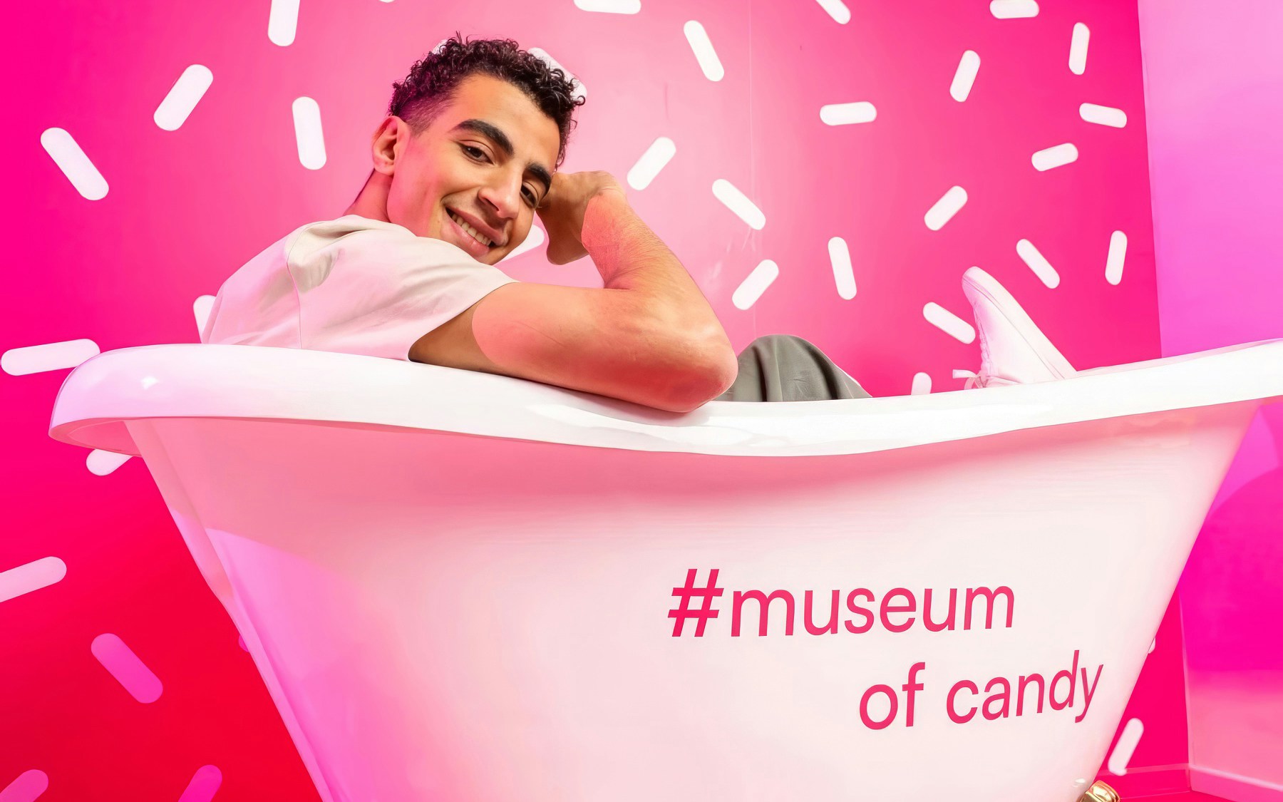 Person sitting in a bathtub at Museum of Candy, Dubai with pink sprinkle backdrop.
