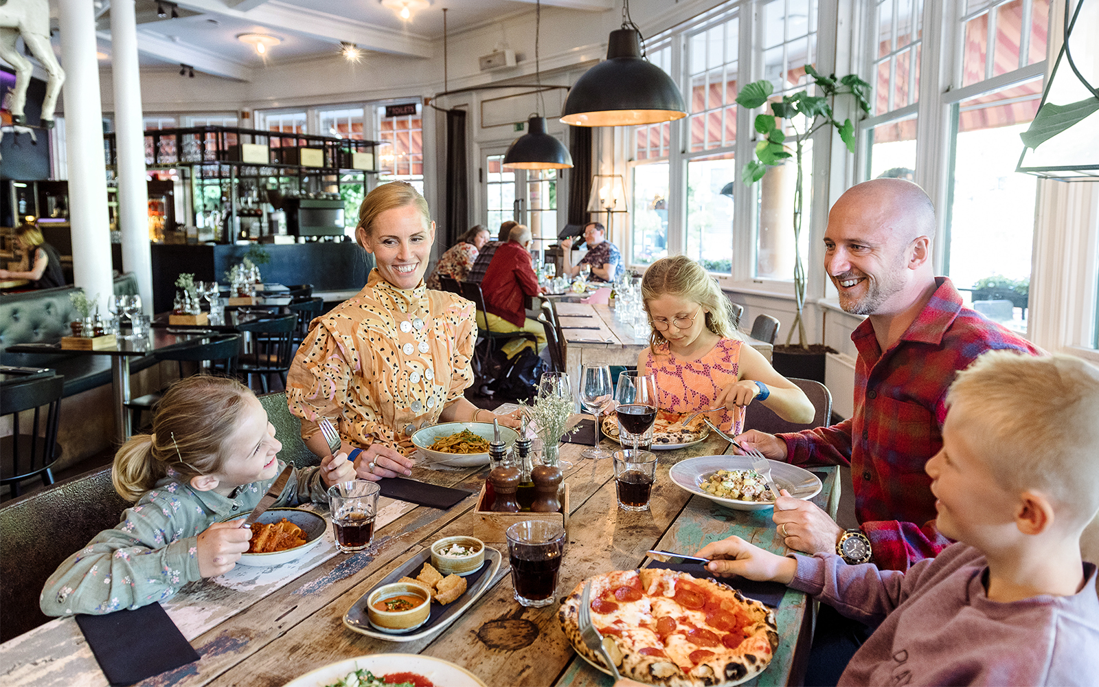 Family dining at a restaurant in Tivoli Gardens, Copenhagen, enjoying pizza and pasta.
