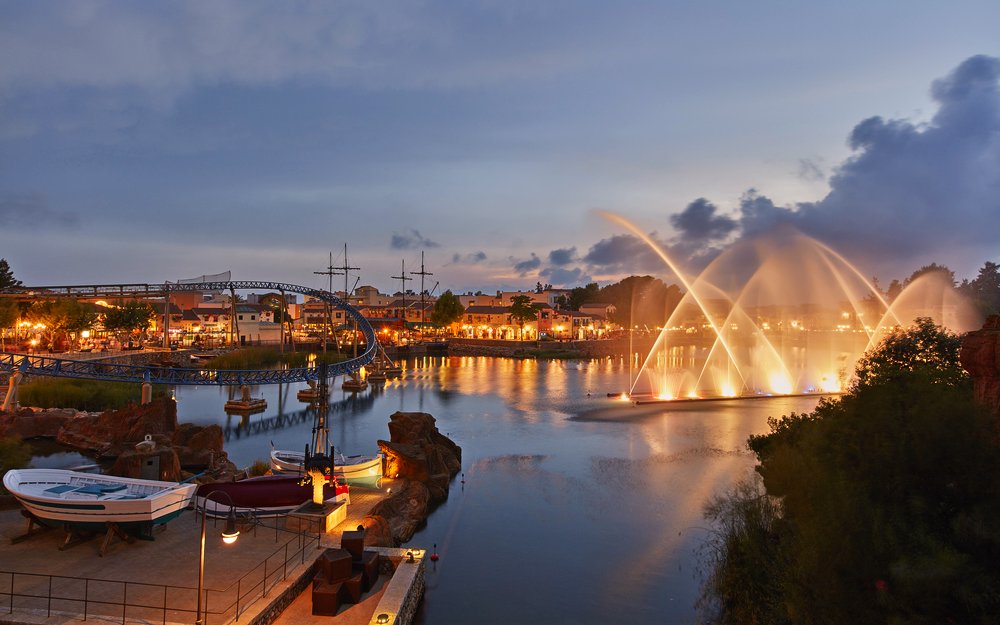 Evening view of PortAventura with illuminated fountains and roller coaster.