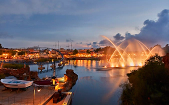 Evening view of PortAventura with illuminated fountains and roller coaster.