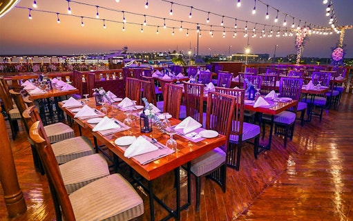 Dining setup on Alishba Dhow Cruise Marina with sunset view and string lights.