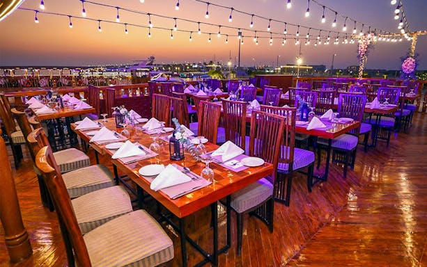 Dining setup on Alishba Dhow Cruise Marina with sunset view and string lights.