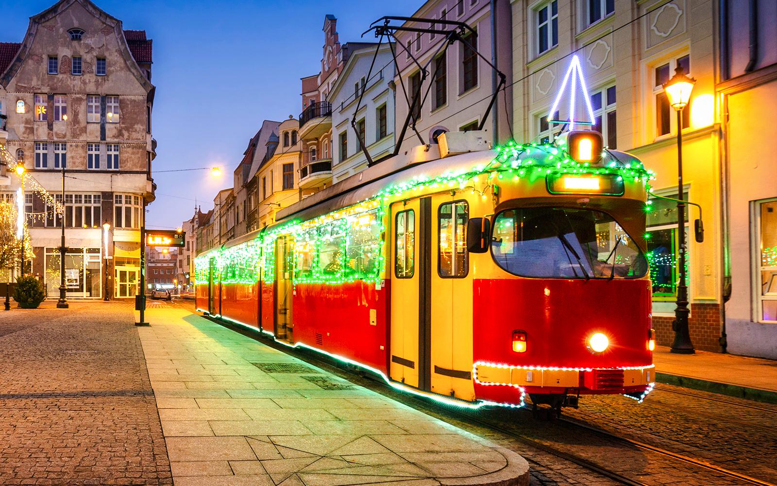 Christmas tram decorated with lights on a city street at dusk.