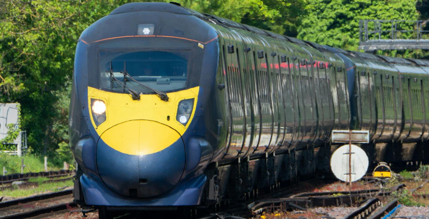 Commuter train approaching Canterbury West Station, UK, surrounded by greenery.