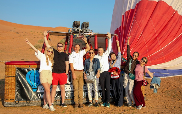 Group of people posing in front of a hot air balloon in Ras Al Khaimah desert.
