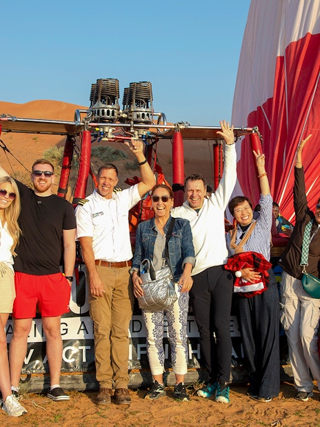 Group of people posing in front of a hot air balloon in Ras Al Khaimah desert.