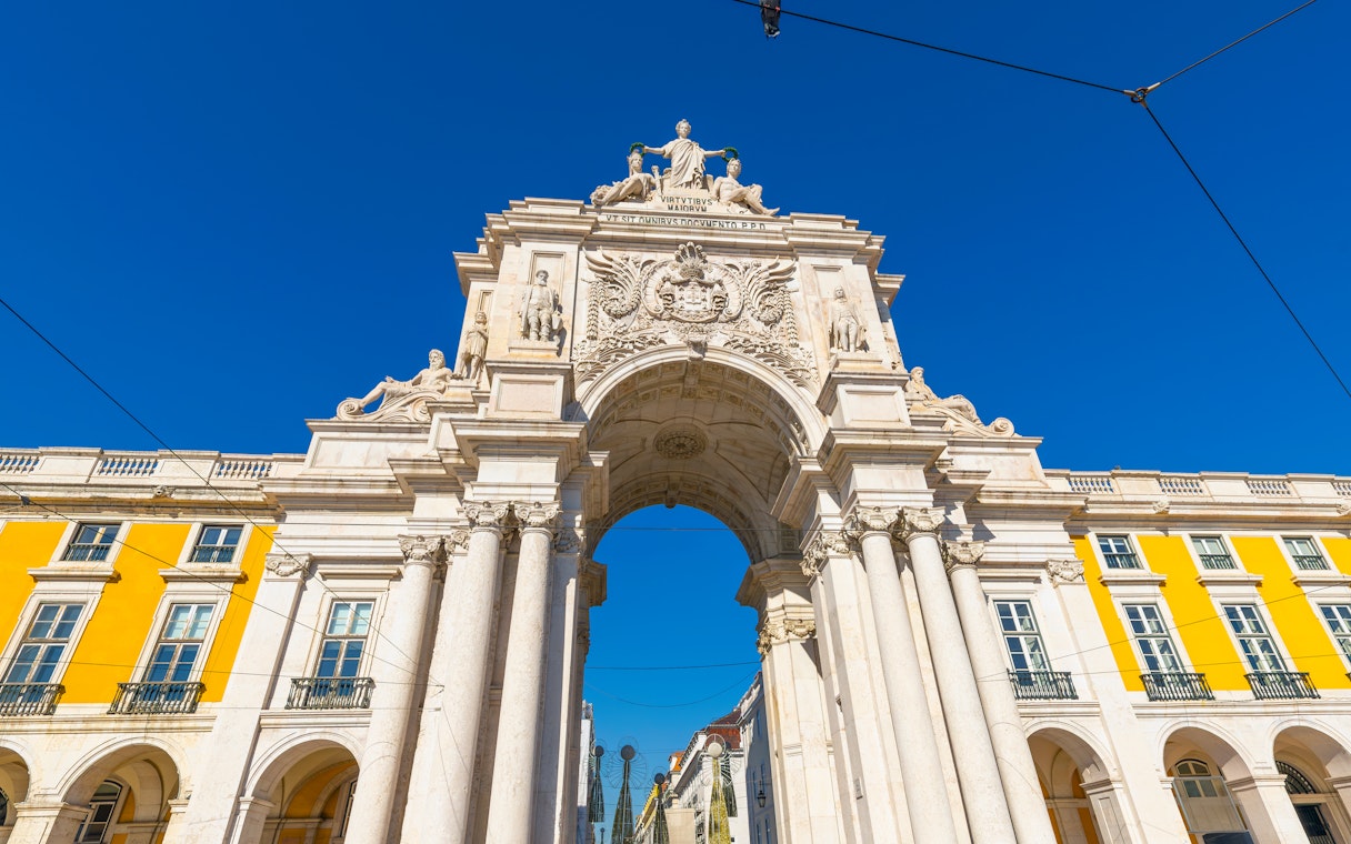 Rua Augusta Arch in Lisbon with detailed sculptures and bright yellow buildings.
