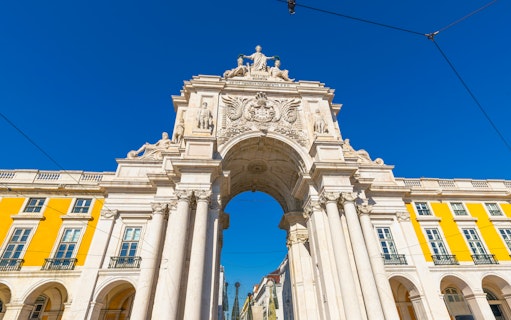 Rua Augusta Arch in Lisbon with detailed sculptures and bright yellow buildings.