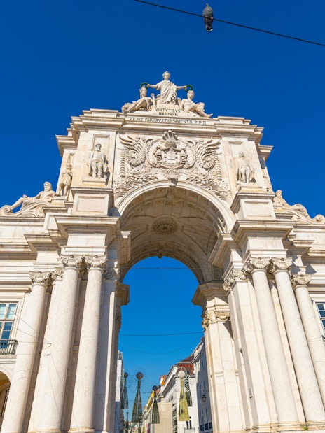 Rua Augusta Arch in Lisbon with detailed sculptures and bright yellow buildings.