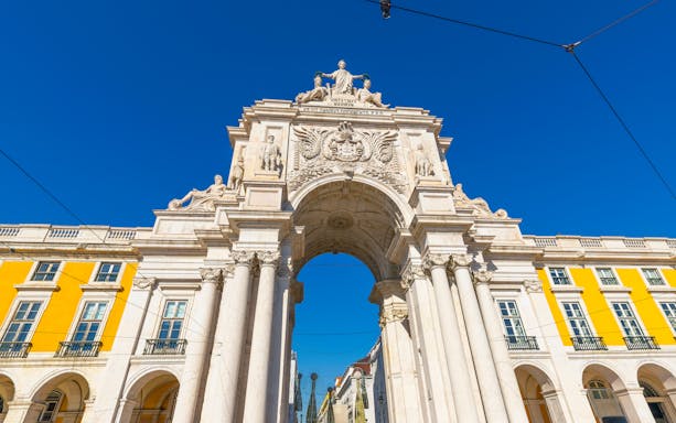 Rua Augusta Arch in Lisbon with detailed sculptures and bright yellow buildings.