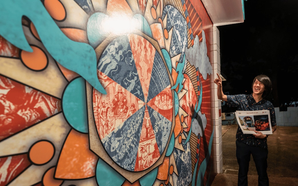 Tour guide gestures at colorful mural at Hell's Museum entrance, Singapore.