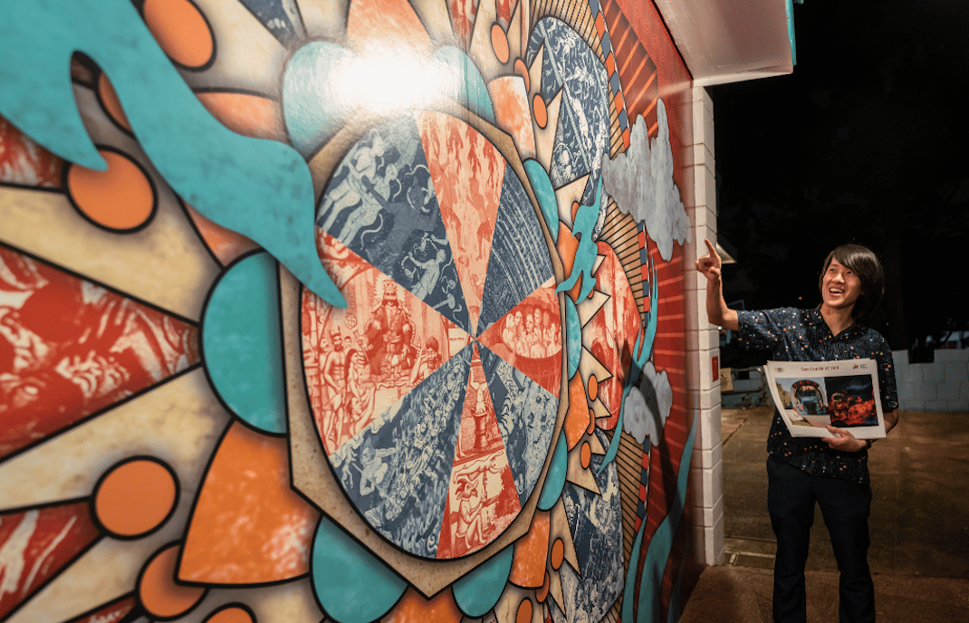 Tour guide gestures at colorful mural at Hell's Museum entrance, Singapore.