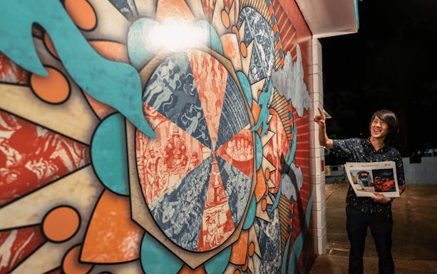 Tour guide gestures at colorful mural at Hell's Museum entrance, Singapore.