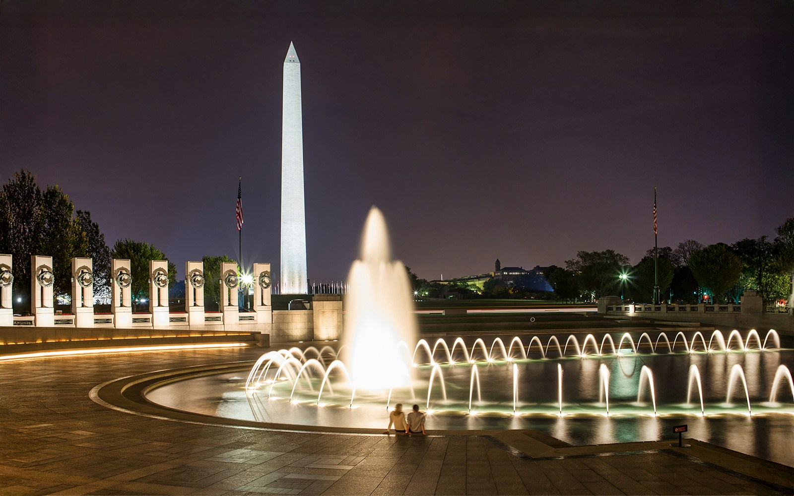 National World War II Memorial fountain and Washington Monument illuminated at night.
