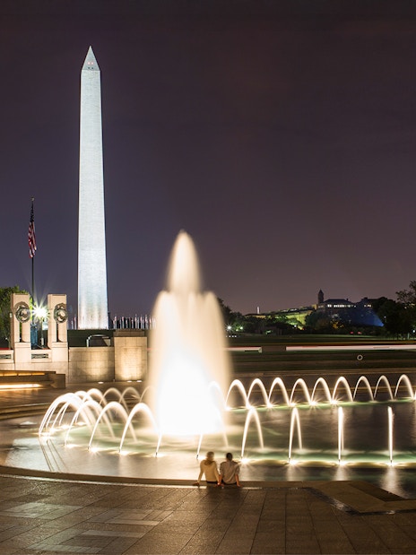 National World War II Memorial fountain and Washington Monument illuminated at night.