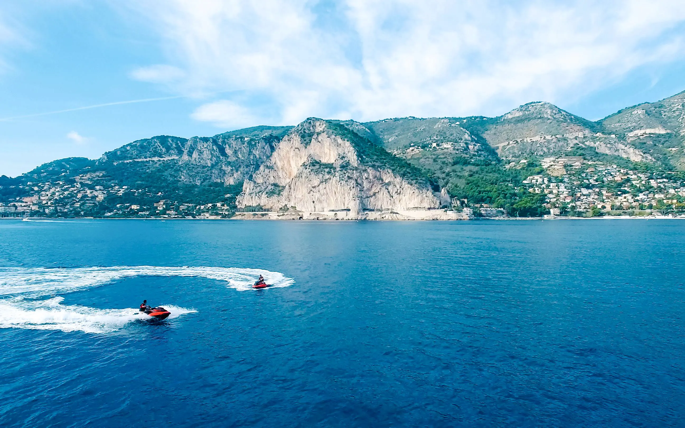 Jetskis on the blue waters of the French Riviera with coastal cliffs in the background.