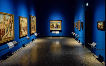 Art gallery room in Pinacoteca di Brera, Milan, featuring Renaissance paintings on blue walls.