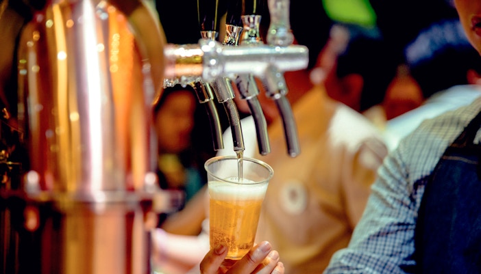 Bartender pouring beer from tap into a plastic cup.