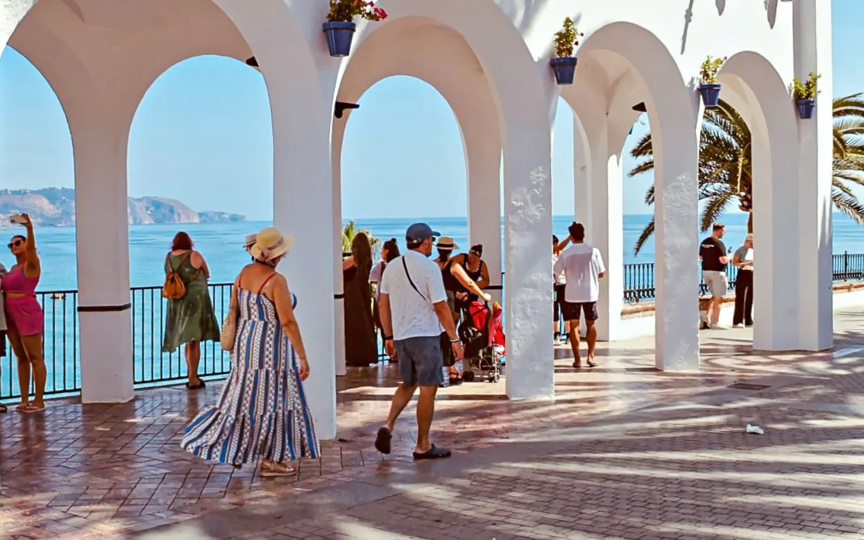 Tourists enjoying the view at Balcon de Europa, Nerja, with ocean and arches in the background.