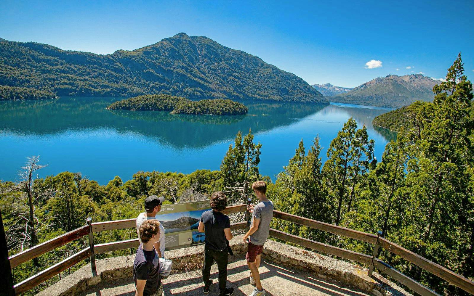 Visitors admiring Lake Mascardi and Patagonian mountains from a scenic viewpoint.